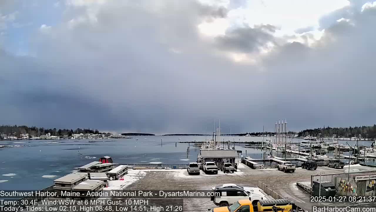 A harbor with numerous boats docked, partially covered in ice, under a mostly cloudy sky.