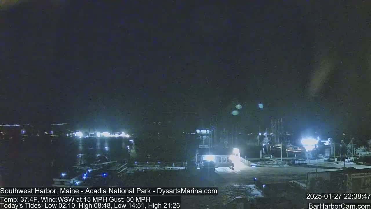 A nighttime harbor scene with boats docked under a dark, clear sky, with a wind of 15 mph gusting to 30 mph.
