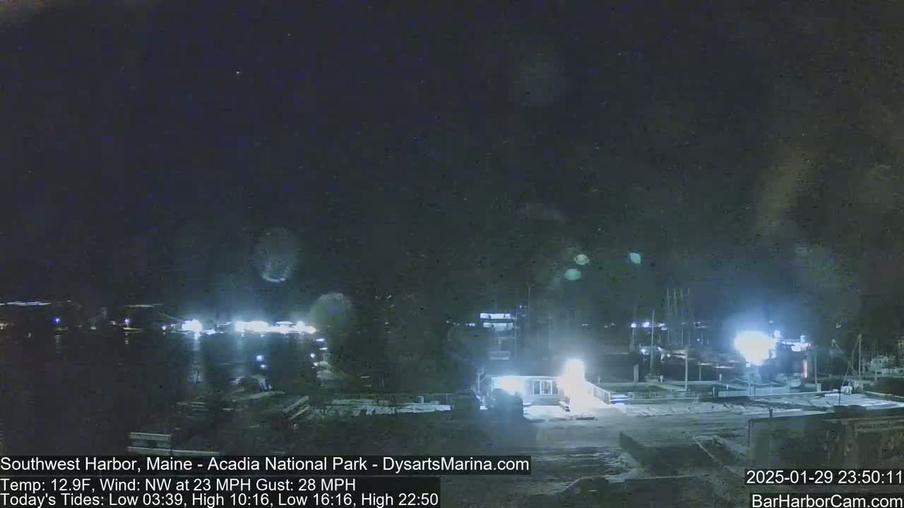 A nighttime harbor scene with boats docked, under a dark sky with a northwest wind at 23 mph and gusts up to 28 mph.