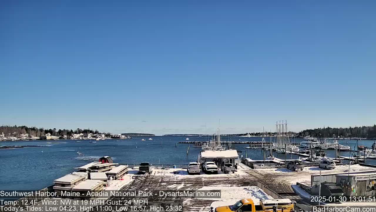 A harbor with boats docked and snow on the ground under a clear blue sky.