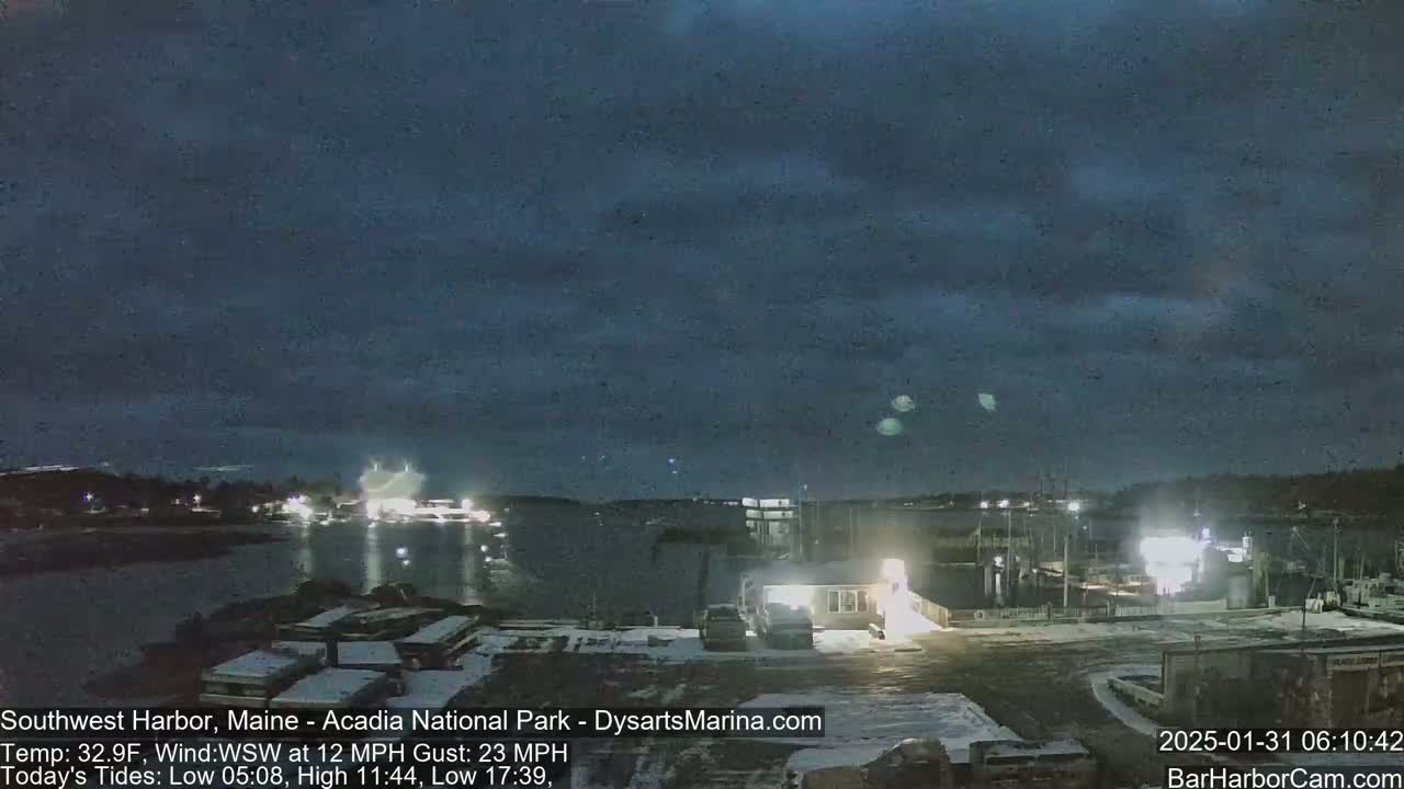 A nighttime view of a snow-covered harbor with boats and buildings under a dark, cloudy sky.