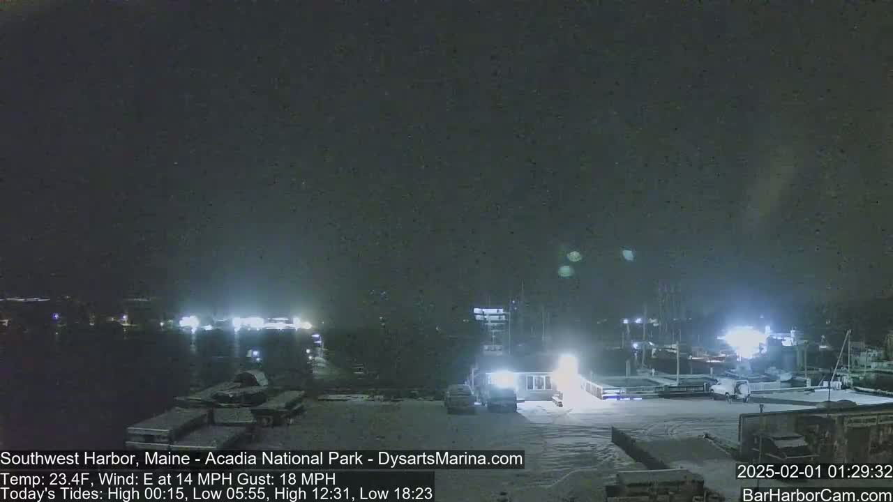 A snow-covered harbor at night with several boats and buildings illuminated under a dark, mostly clear sky.