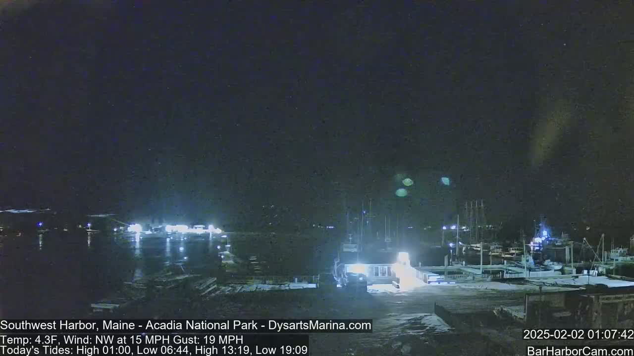A nighttime harbor scene shows docked boats and a building under a dark, clear sky with a northwest wind.
