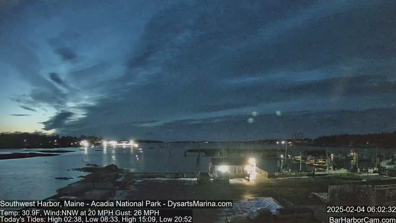 A twilight view of a harbor with boats and a marina under a mostly cloudy, dark blue sky.