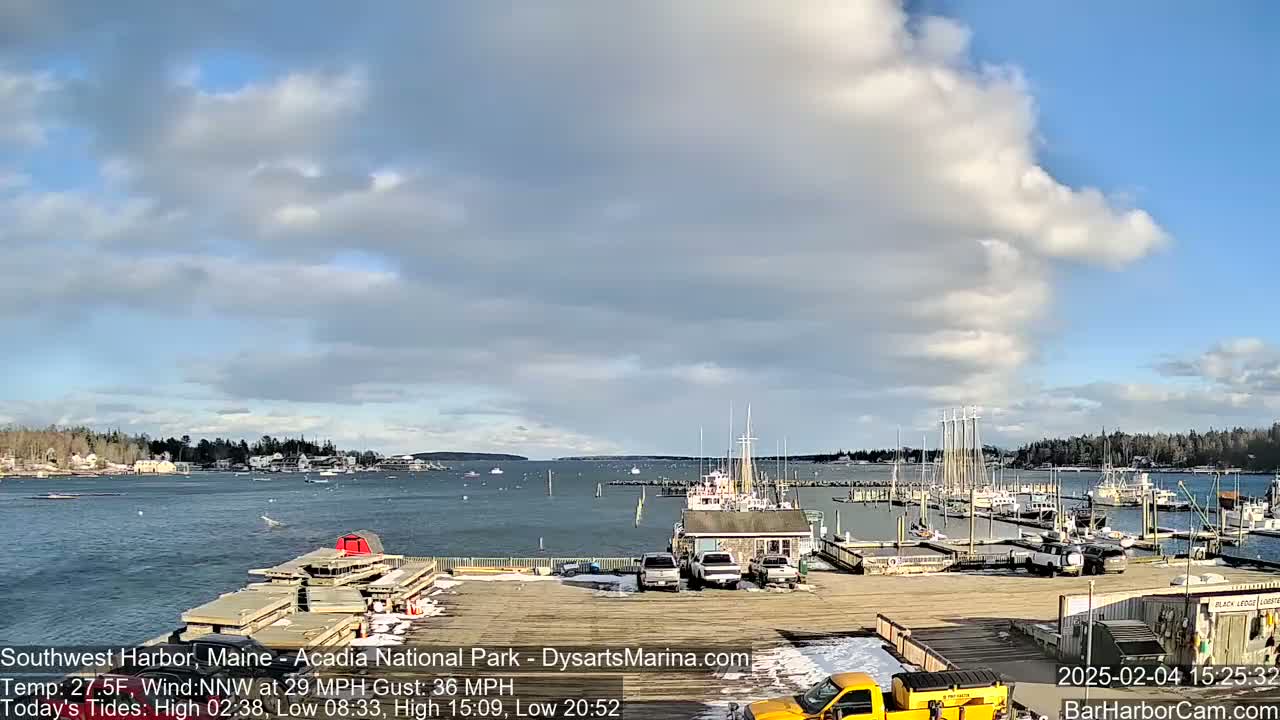 A harbor filled with boats and docked ships is seen under a partly cloudy sky.
