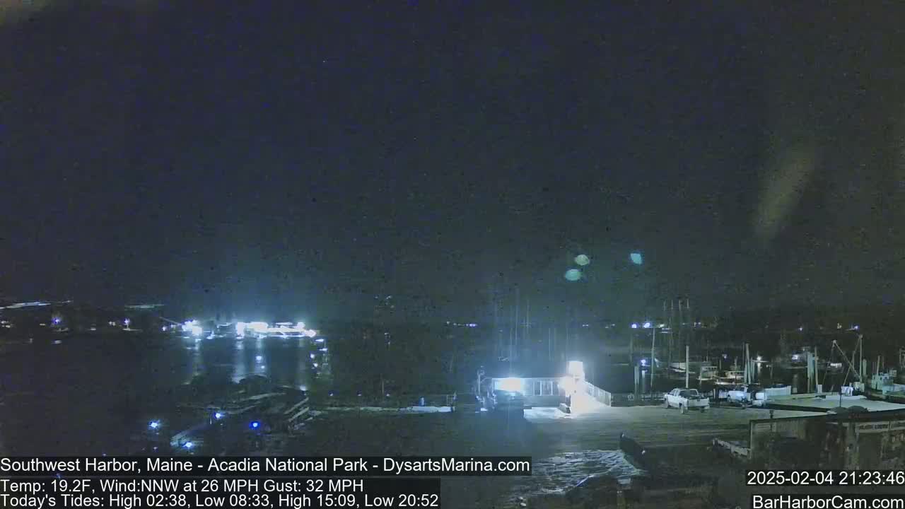 A nighttime harbor scene with docked boats under a dark sky, with a moderate northwest wind.