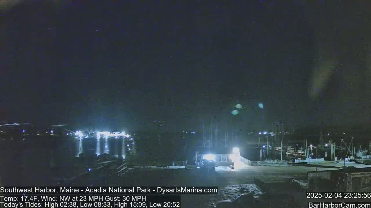 A nighttime view of a harbor with boats and buildings under a dark, clear sky, with a strong northwest wind.