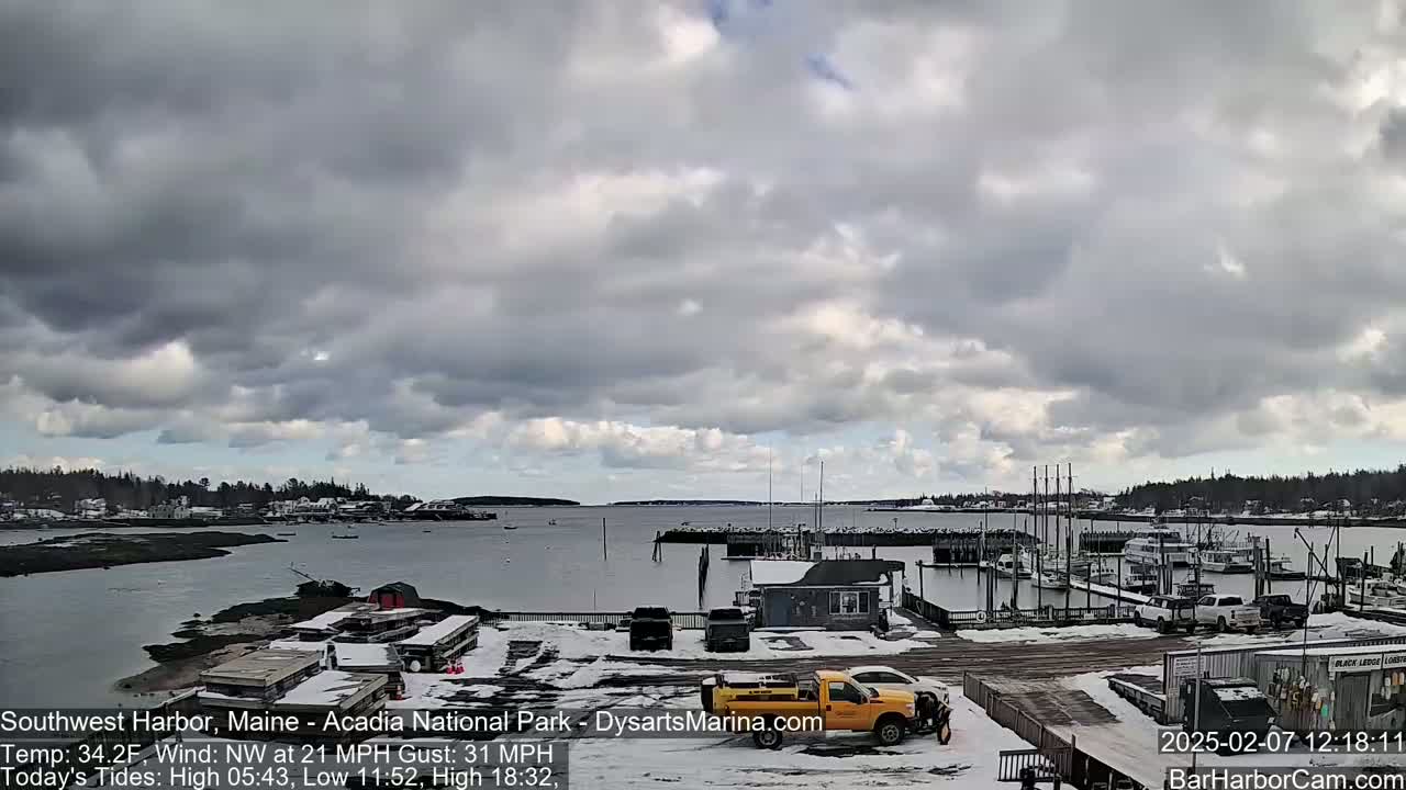 A snow-covered harbor with boats docked, a yellow pickup truck, and a partly cloudy sky.