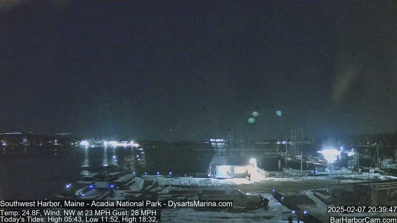A nighttime view of a harbor with snow on the ground, under a dark sky with a few faint lights visible in the distance.