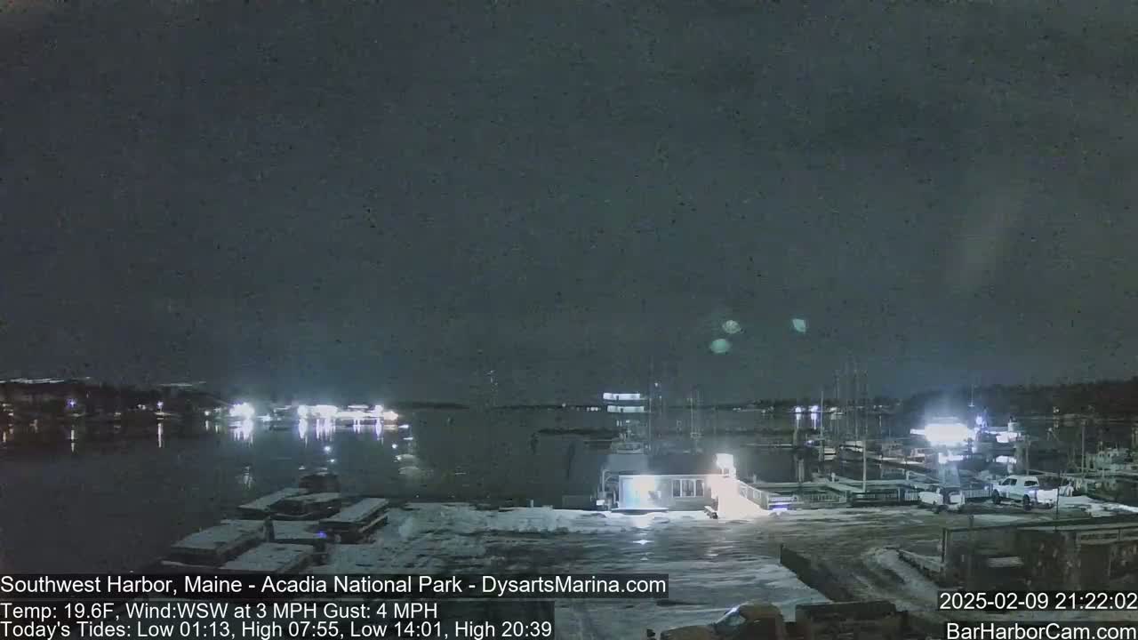 A nighttime view of a snow-covered harbor with boats docked, under a dark, clear sky.