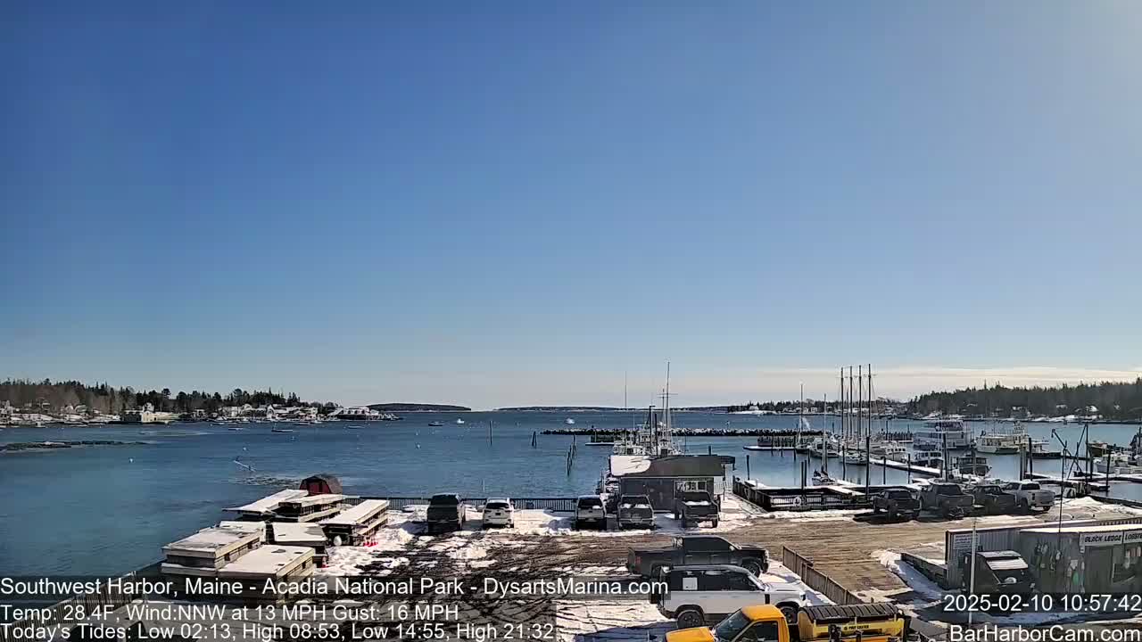 A harbor filled with boats and cars under a clear blue sky, with some snow on the ground.