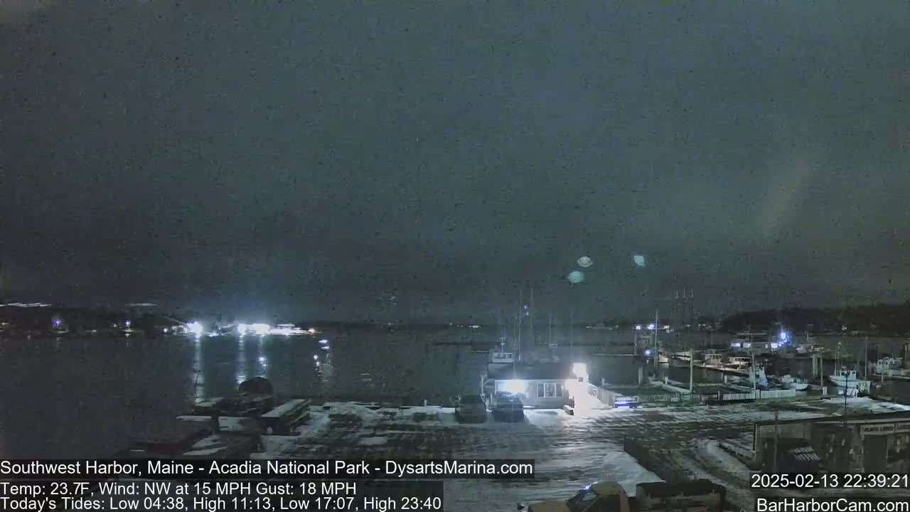 A nighttime view of a snow-covered harbor with boats docked under a dark, overcast sky.