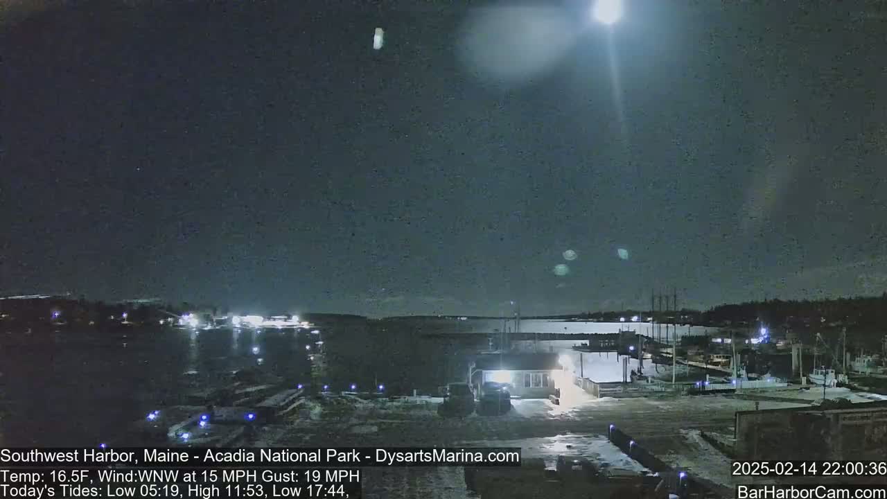 A nighttime view of a harbor with a bright moon and some boats, under windy conditions.