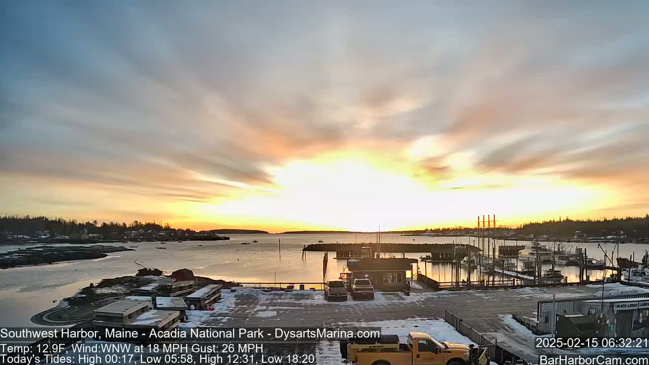 A harbor with boats docked at sunrise under a partly cloudy sky with a 18 mph wind and gusts up to 26 mph.