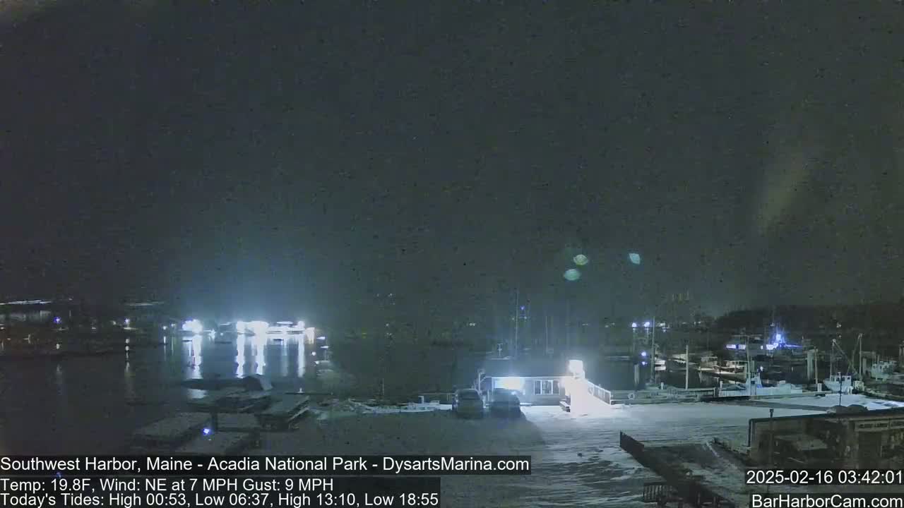 A snow-covered marina at night with a dark, overcast sky and boats illuminated by lights.