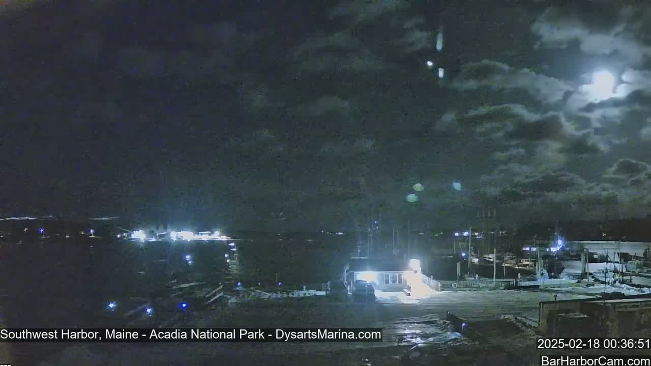A nighttime view of a harbor with a partially cloudy sky and a bright moon.