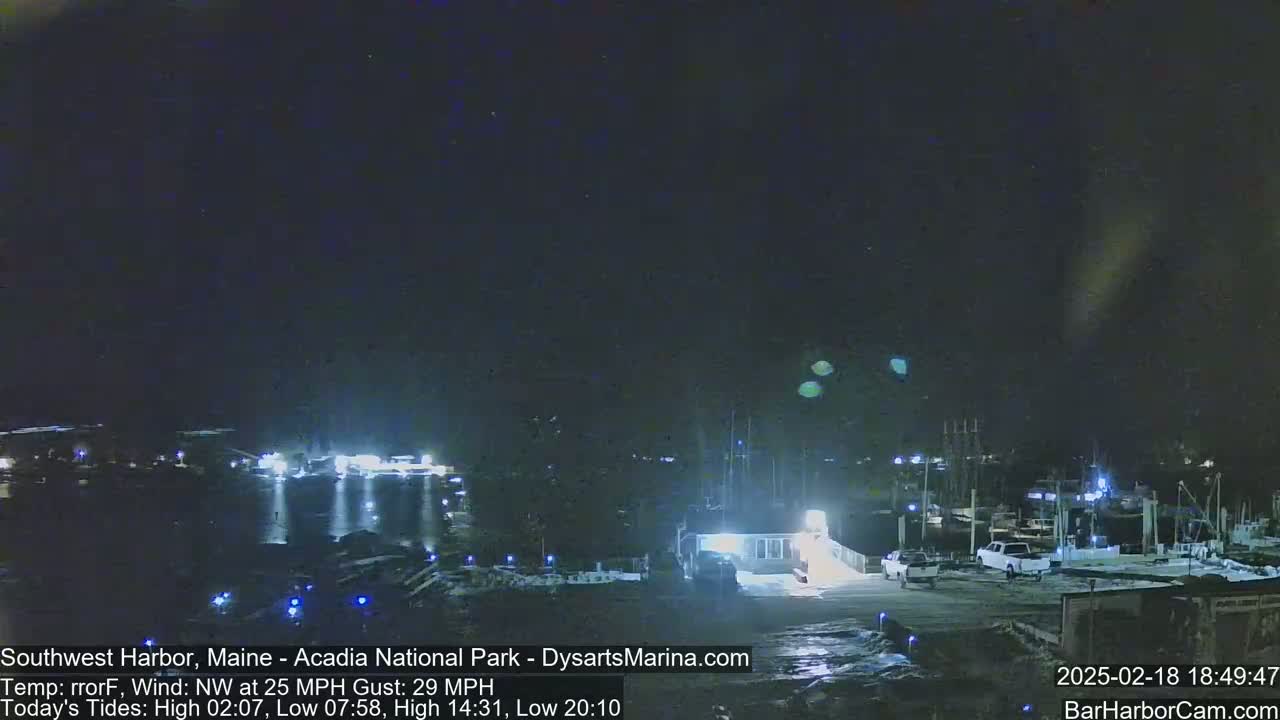 A nighttime harbor scene with numerous boats and vehicles under a dark, clear sky, with a northwest wind at 25 mph and gusts up to 29 mph.