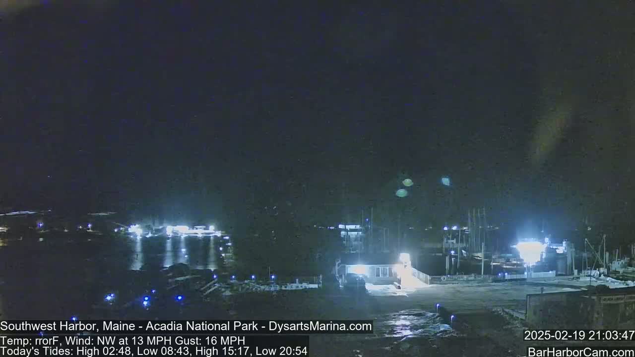 A nighttime view of a harbor with boats docked, under a dark sky with a northwest wind.