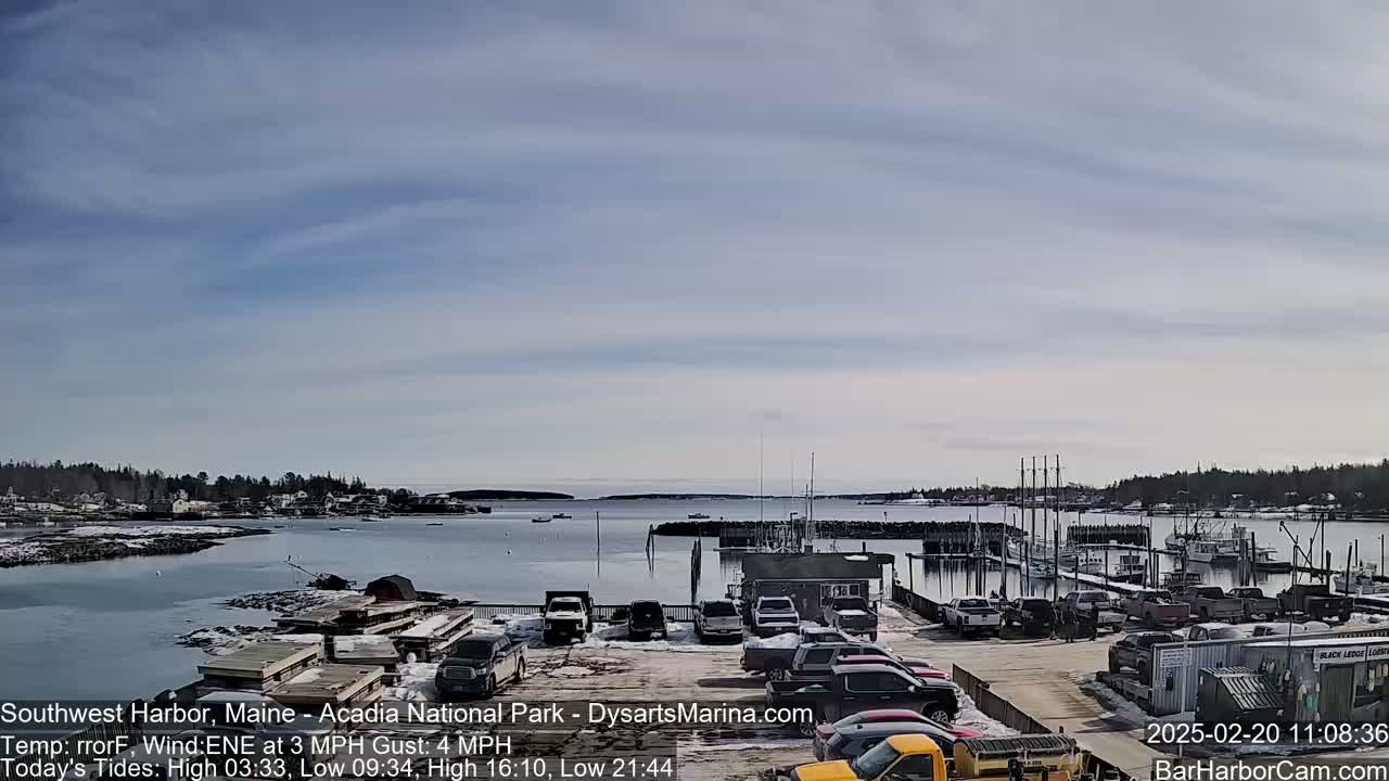 A harbor filled with docked boats and cars parked in a lot under a partly cloudy sky.