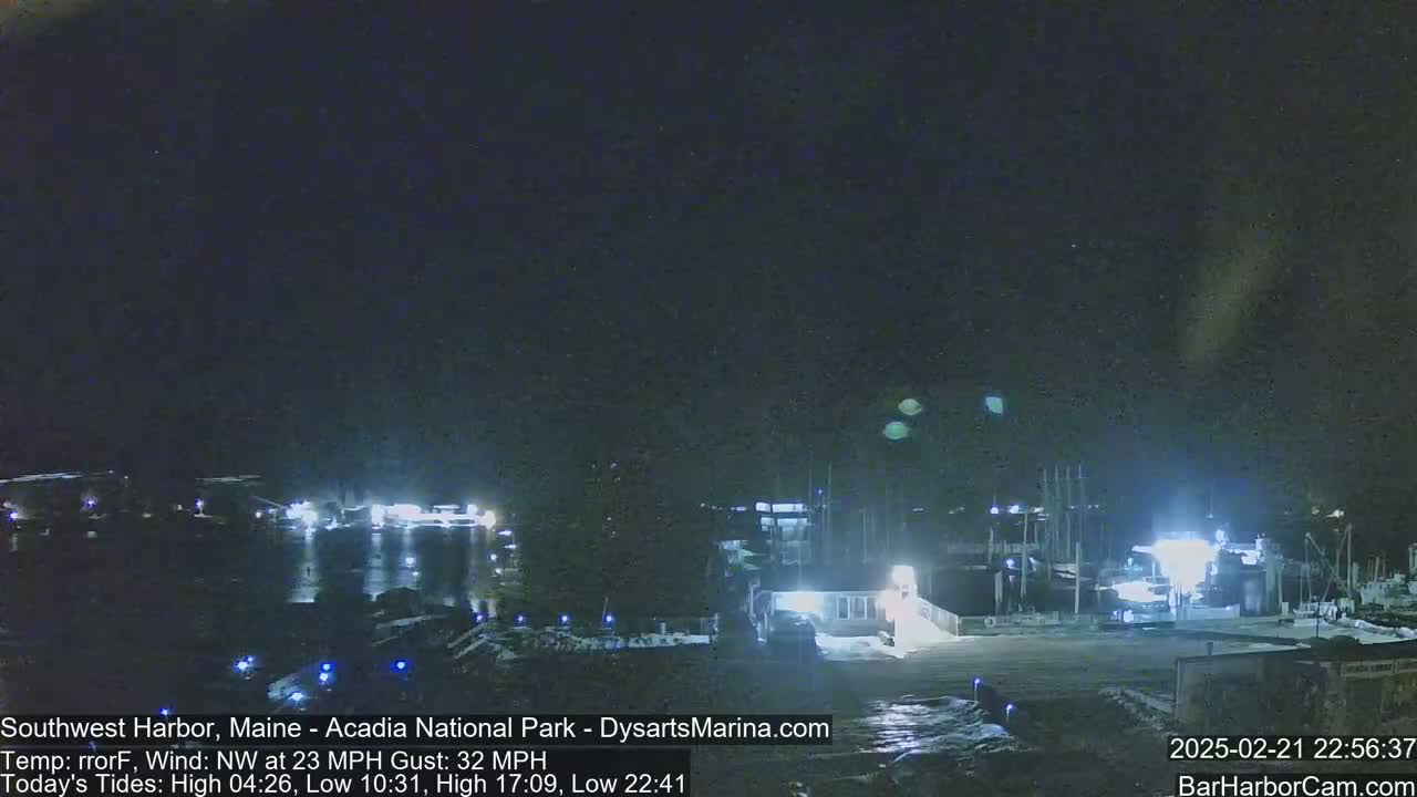 A nighttime harbor scene with boats docked under a dark, clear sky and a northwest wind of 23 mph gusting to 32 mph.