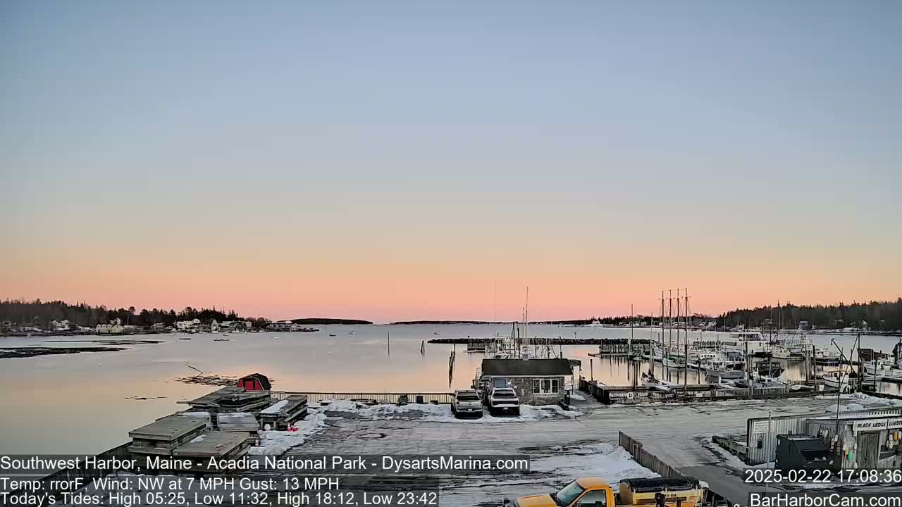 A harbor with boats docked at a marina is seen at sunset under a partly cloudy sky.