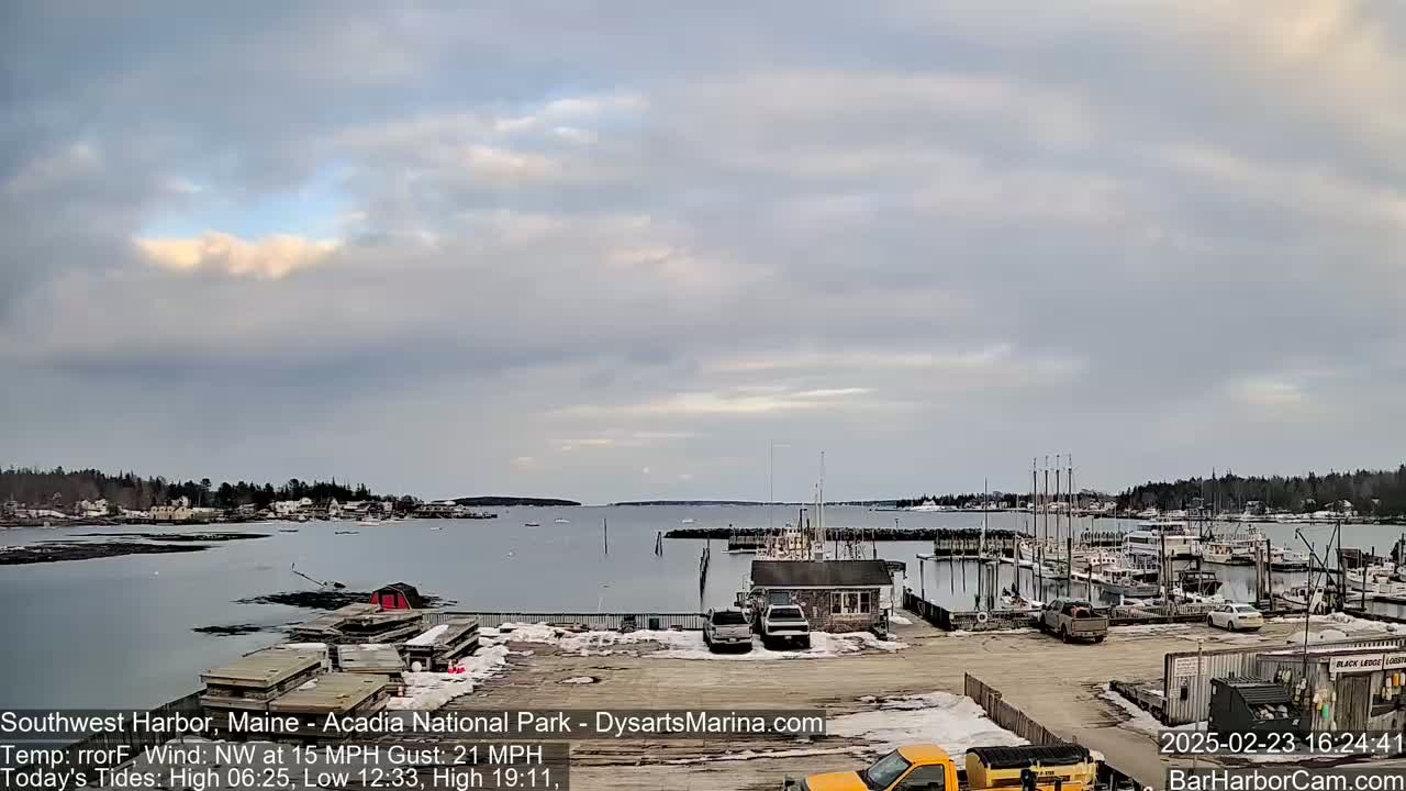 A harbor filled with boats and a few vehicles is seen under a mostly cloudy sky.