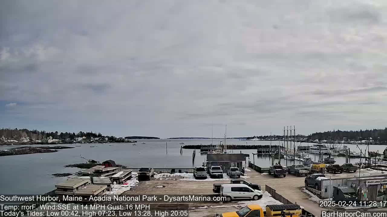 A calm harbor with boats docked at a marina, under a mostly cloudy sky.