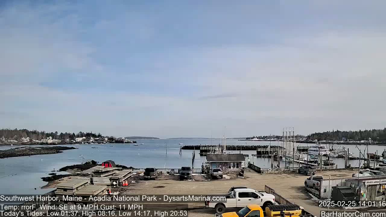 A harbor with docked boats and a few cars in a parking lot is visible under a partly cloudy sky.