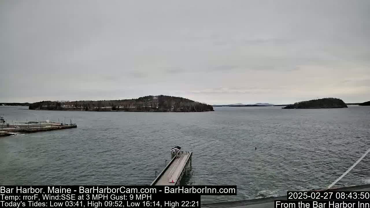 A long pier extends into a calm body of water under an overcast sky, with islands and a shoreline visible in the distance.