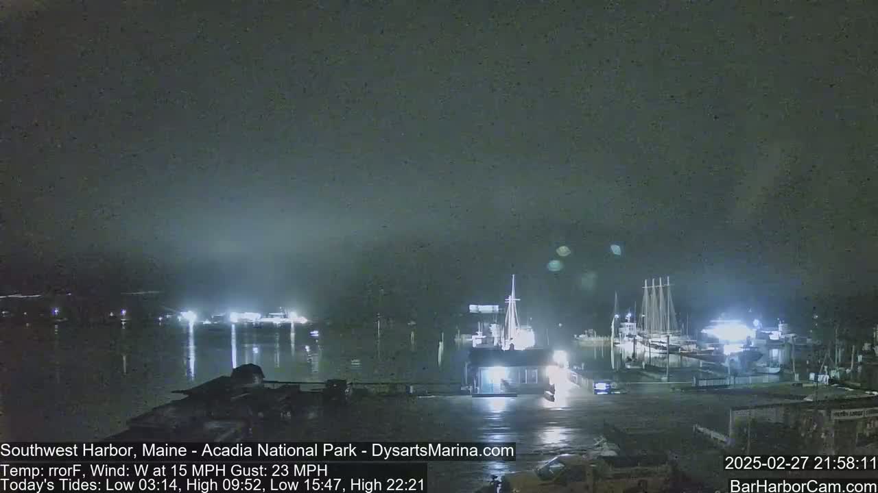 A nighttime harbor scene with boats docked under a dark, overcast sky and a 15 mph wind with gusts up to 23 mph.