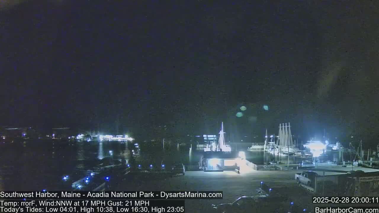 A nighttime view of a harbor with boats docked, under a dark, clear sky with a northwest wind.