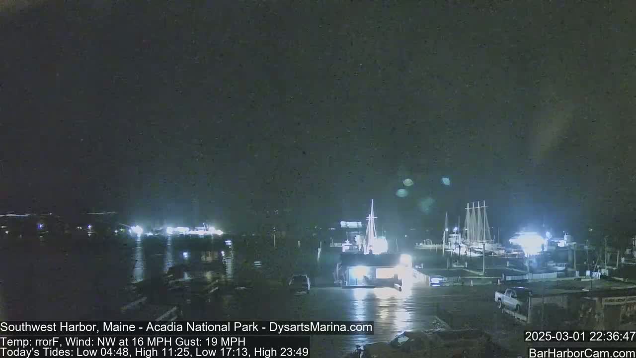 A nighttime view of a harbor with boats docked, under a dark sky with a northwest wind.