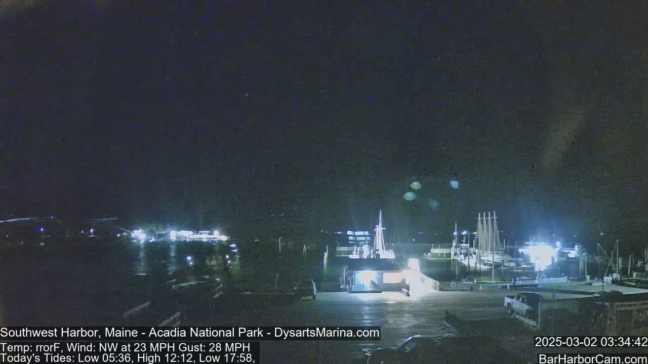 A nighttime harbor scene with several boats docked under a dark sky and a northwest wind blowing at 23 mph with gusts up to 28 mph.