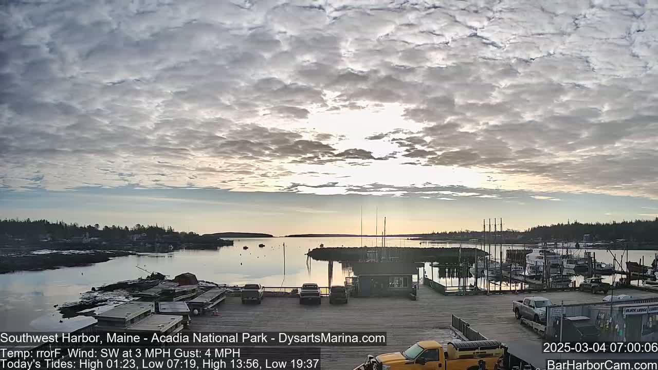 A calm harbor filled with boats under a mostly cloudy sky at sunrise.
