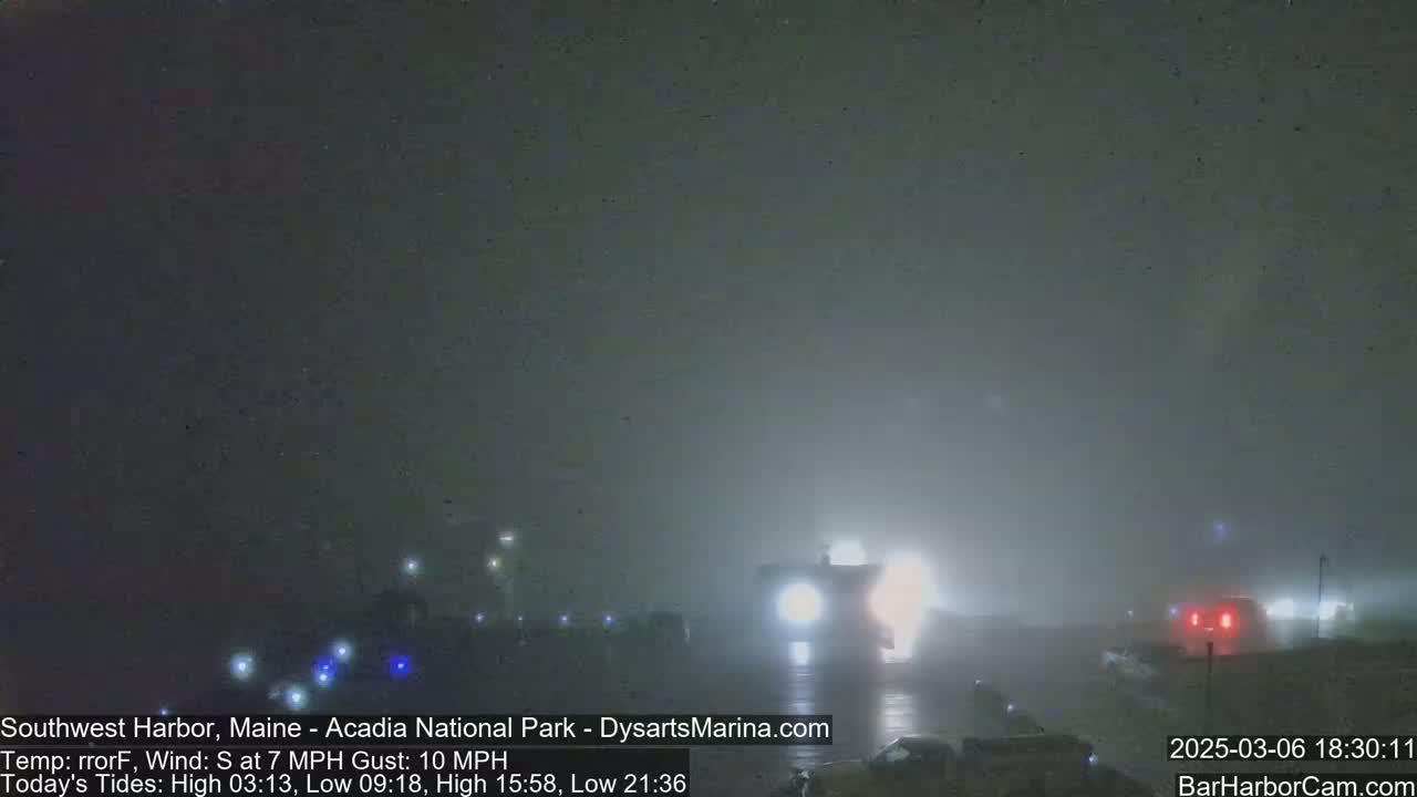 A foggy night scene shows several vehicles with headlights on driving along a road.
