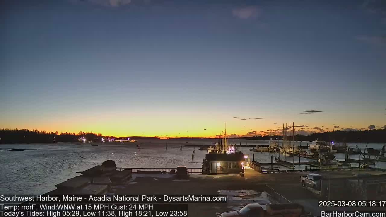 A sunset over a harbor filled with boats, under a clear sky with a WNW wind at 15 mph and gusts up to 24 mph.