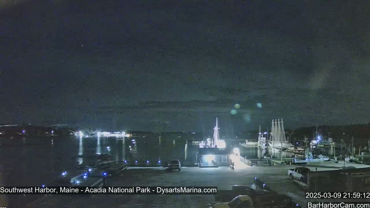 A nighttime harbor scene shows boats docked at a marina under a mostly clear, dark sky.