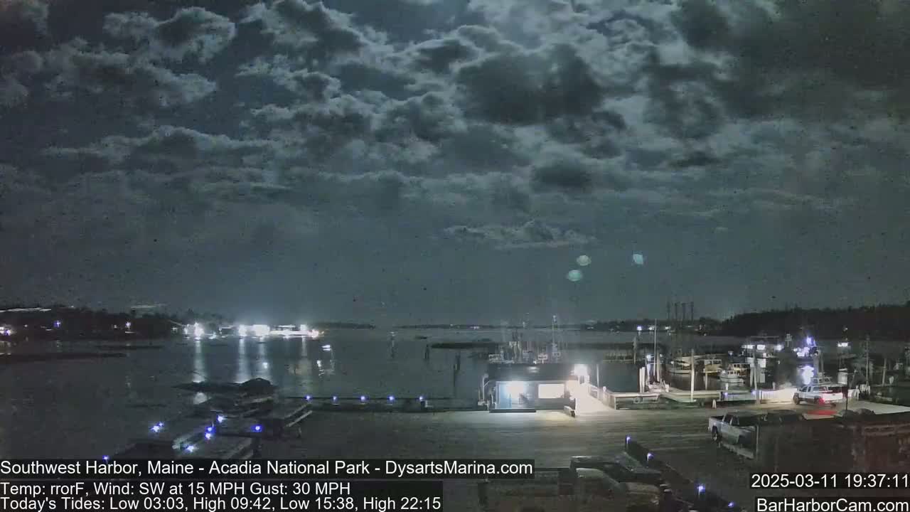A nighttime view of a harbor with boats and a building under a partly cloudy sky.