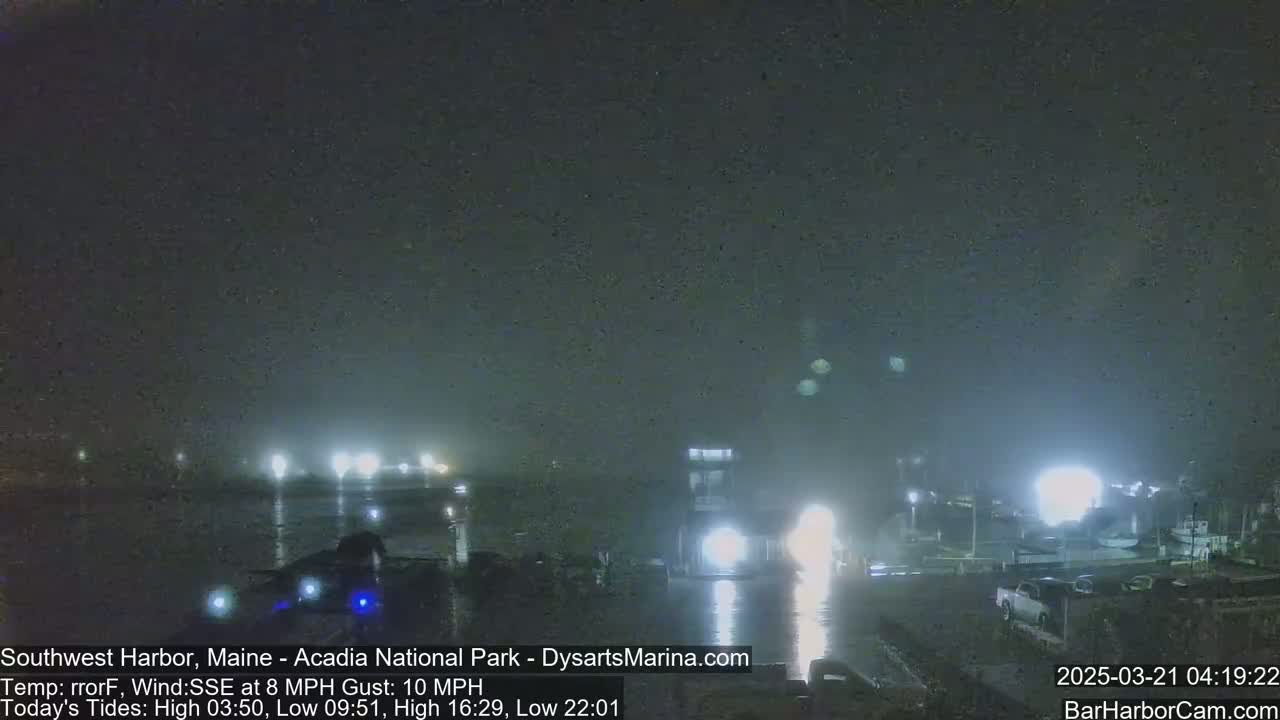 A nighttime harbor scene with fog, showing lights reflecting on the water and several boats.