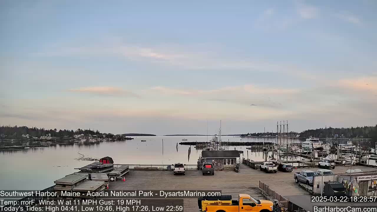 A calm harbor with numerous boats docked, under a mostly clear, light-blue sky at dusk.
