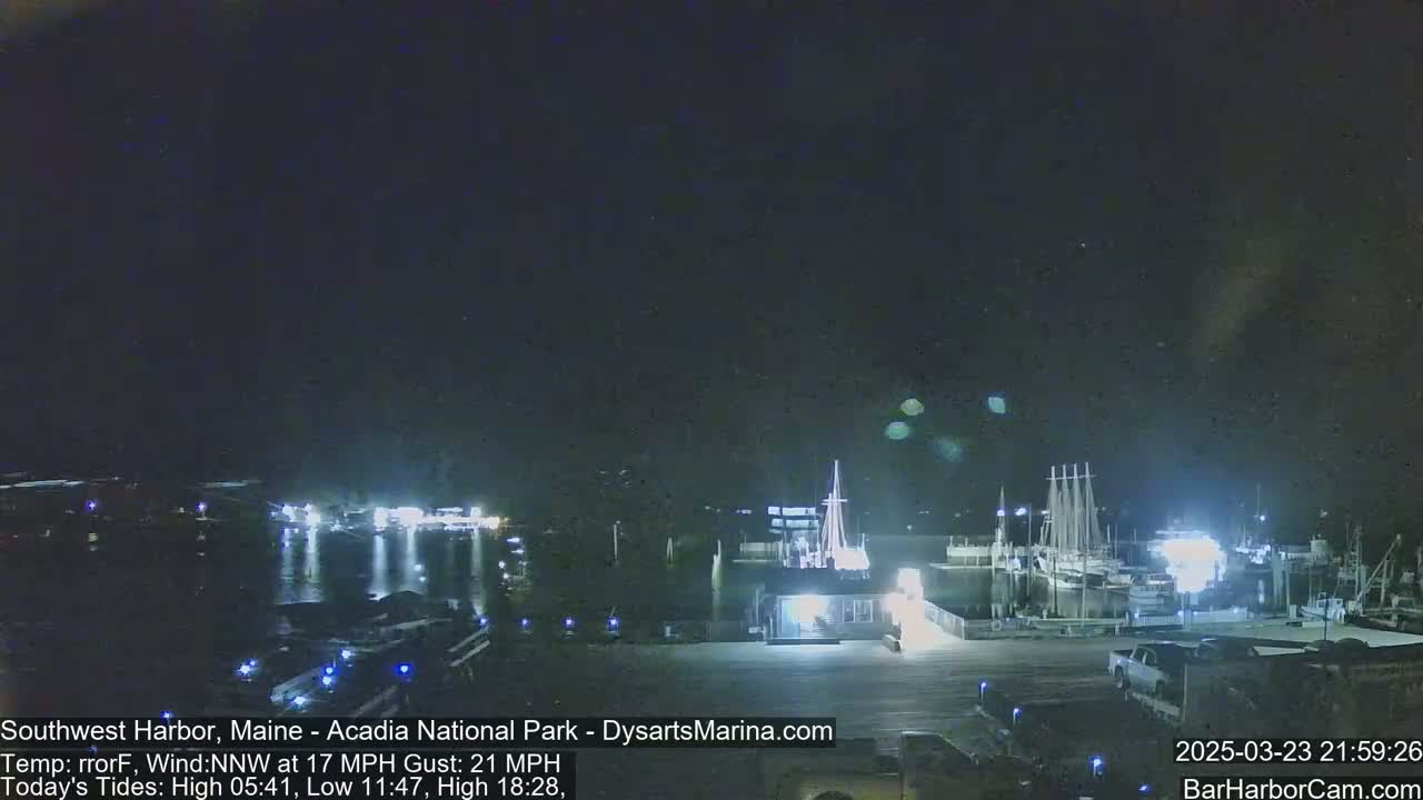 A nighttime harbor scene with boats docked, illuminated by lights under a dark sky with a northwest wind.