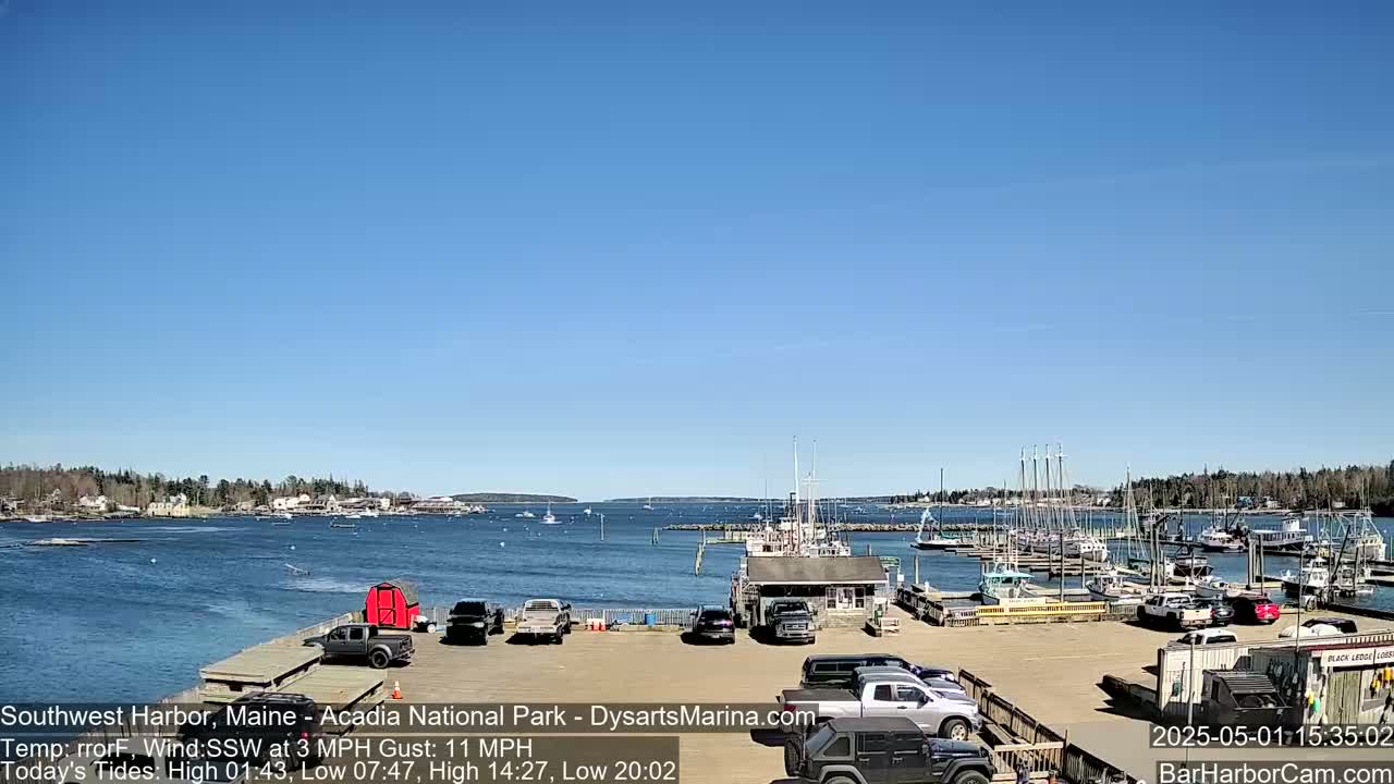 A harbor filled with boats and parked cars is viewed on a sunny day under a clear blue sky.