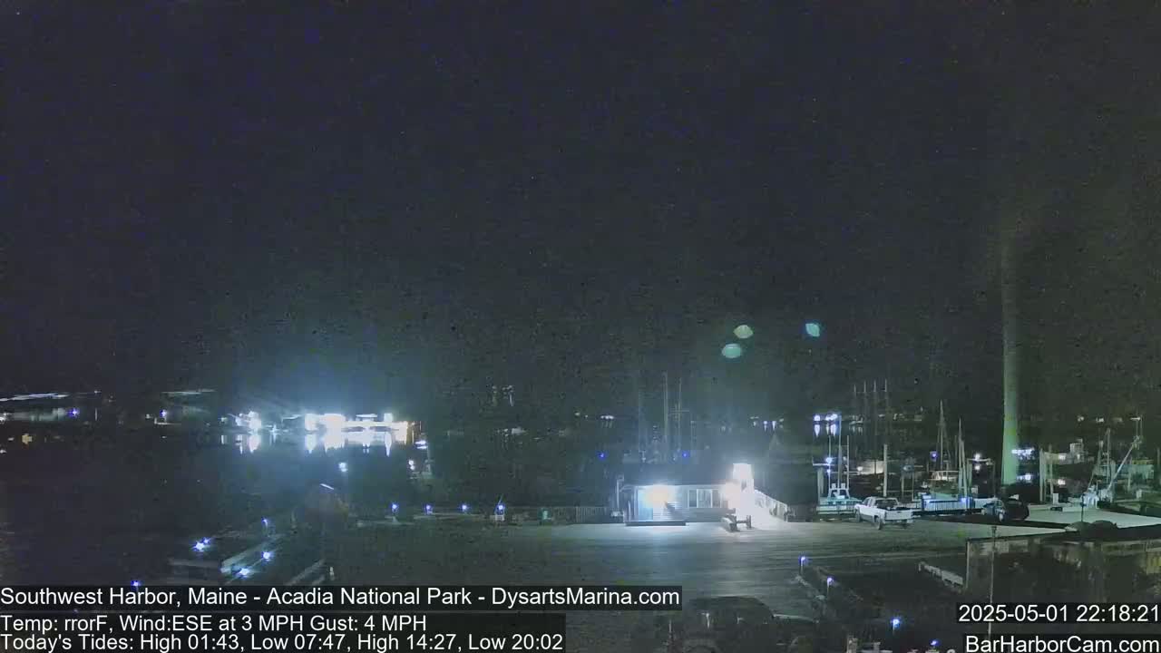 A nighttime view of a harbor with boats docked, under a dark sky with a few faint lights visible in the distance.
