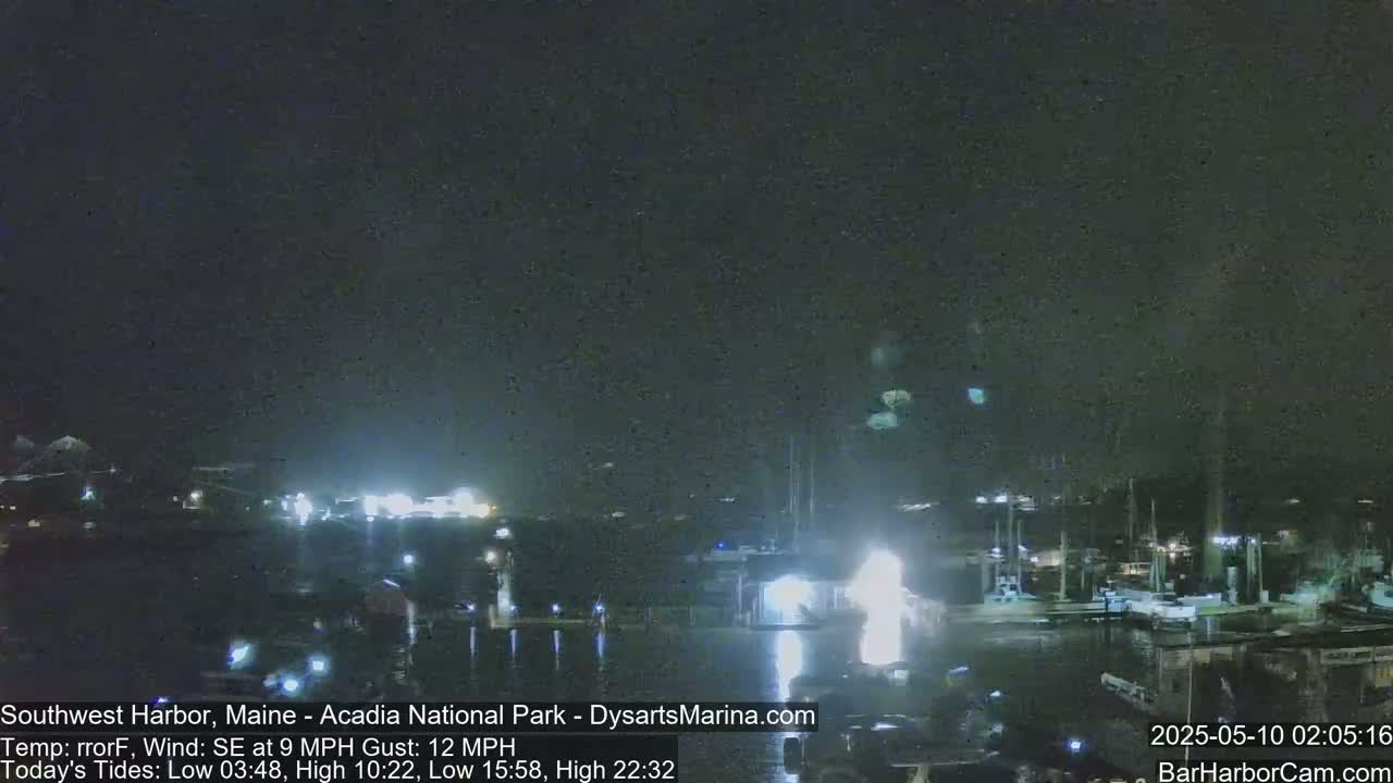 A nighttime view of a harbor with boats docked, under a dark sky with a southeast wind.