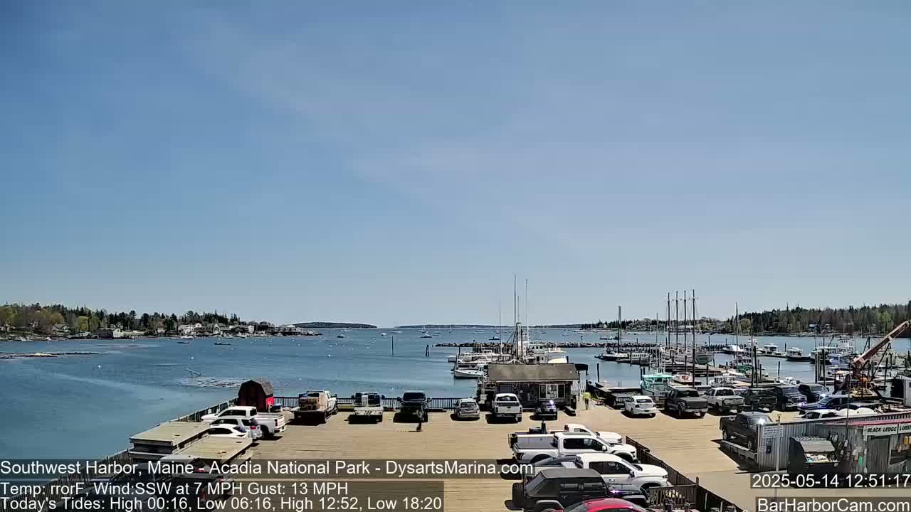 A harbor filled with boats and cars parked in a lot under a clear blue sky.