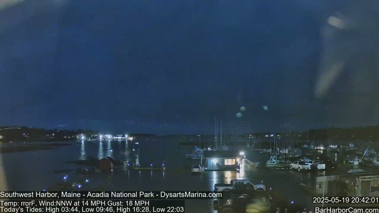 A nighttime view of a harbor with boats and buildings under a dark, mostly clear sky with a northwest wind.