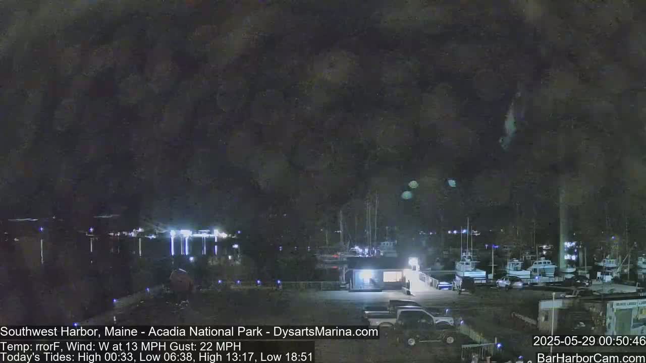 A nighttime view of a harbor with boats docked, under a dark, cloudy sky with a southwest wind.