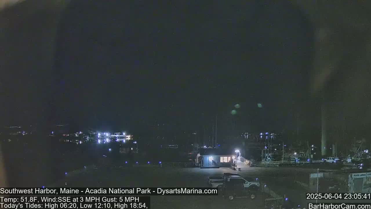 A nighttime view of a harbor with boats and a building, under a dark sky with a few indistinct lights in the distance.