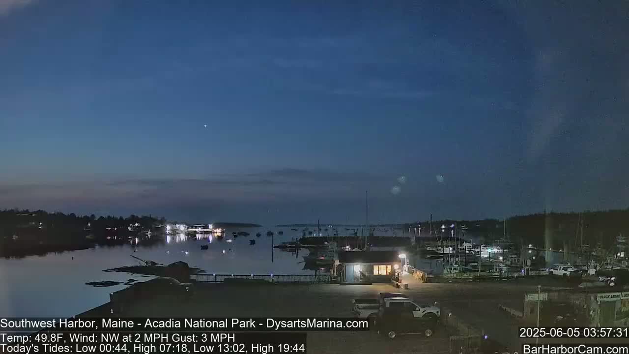 A mostly clear twilight sky over a calm harbor filled with docked boats and a few cars in a parking lot.