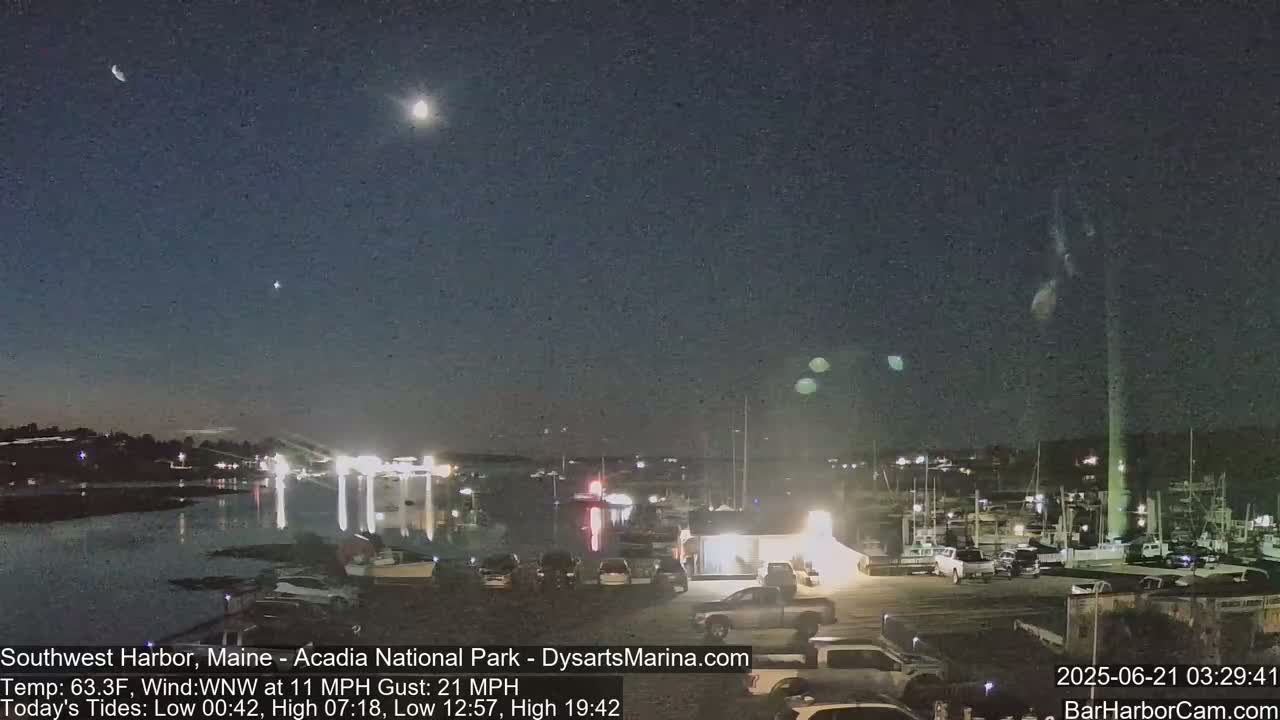 A nighttime harbor scene under a partly cloudy sky shows a crescent moon and stars above a marina with parked cars and boats.